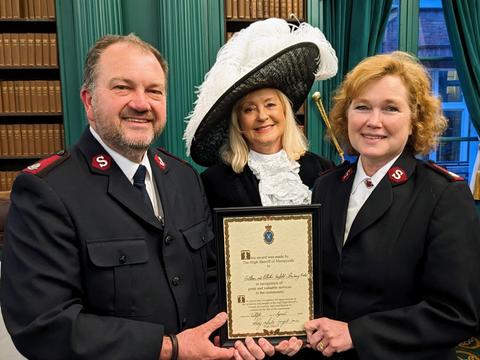 3 people stand holding certificate from High Sheriff of Merseyside 